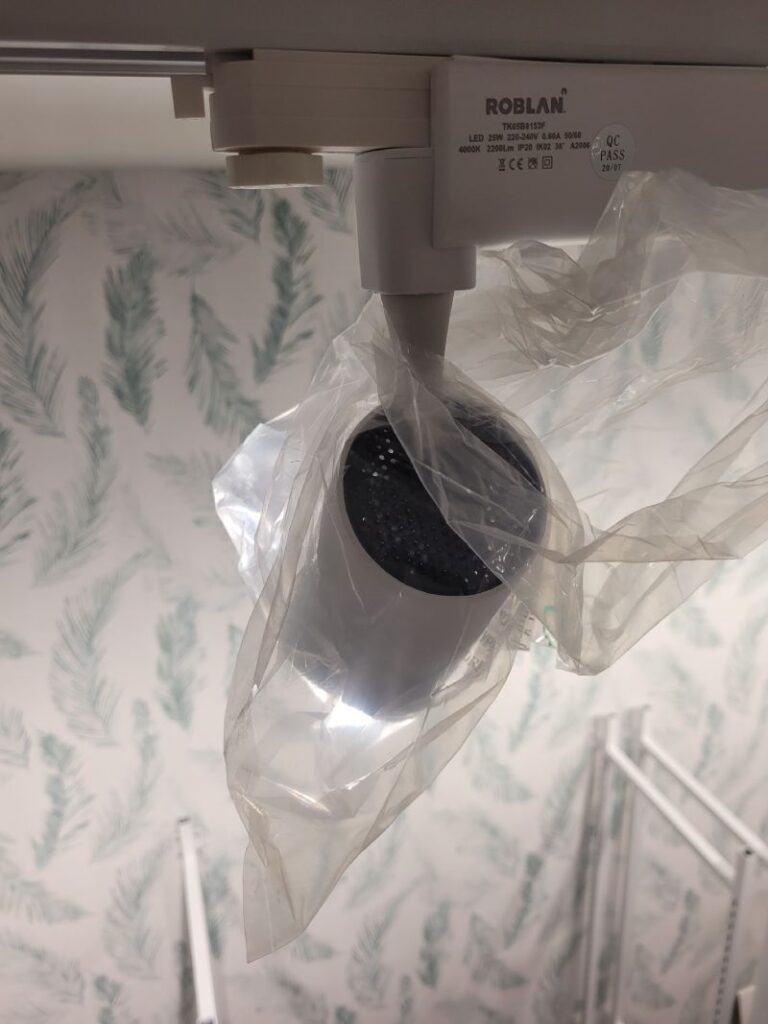 Focos LED de la marca Roblan instalados en un riel, cubiertos con plástico protector. La imagen muestra una vista cercana de los focos, con un fondo borroso que sugiere un área en proceso de instalación o renovación.