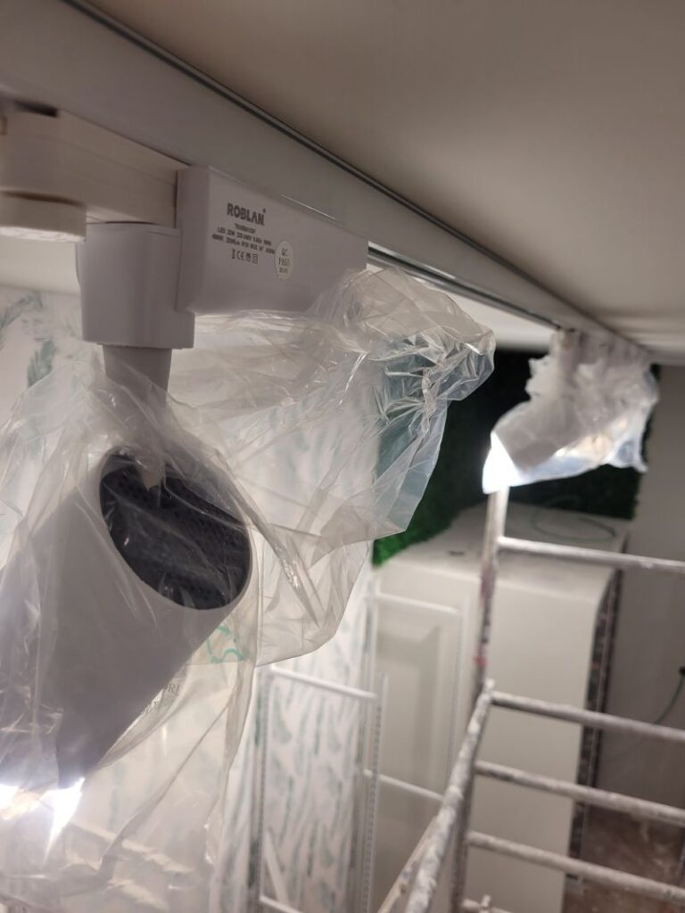 Focos LED de la marca Roblan instalados en un riel, cubiertos con plástico protector. La imagen muestra una vista cercana de los focos, con un fondo borroso que sugiere un área en proceso de instalación o renovación.