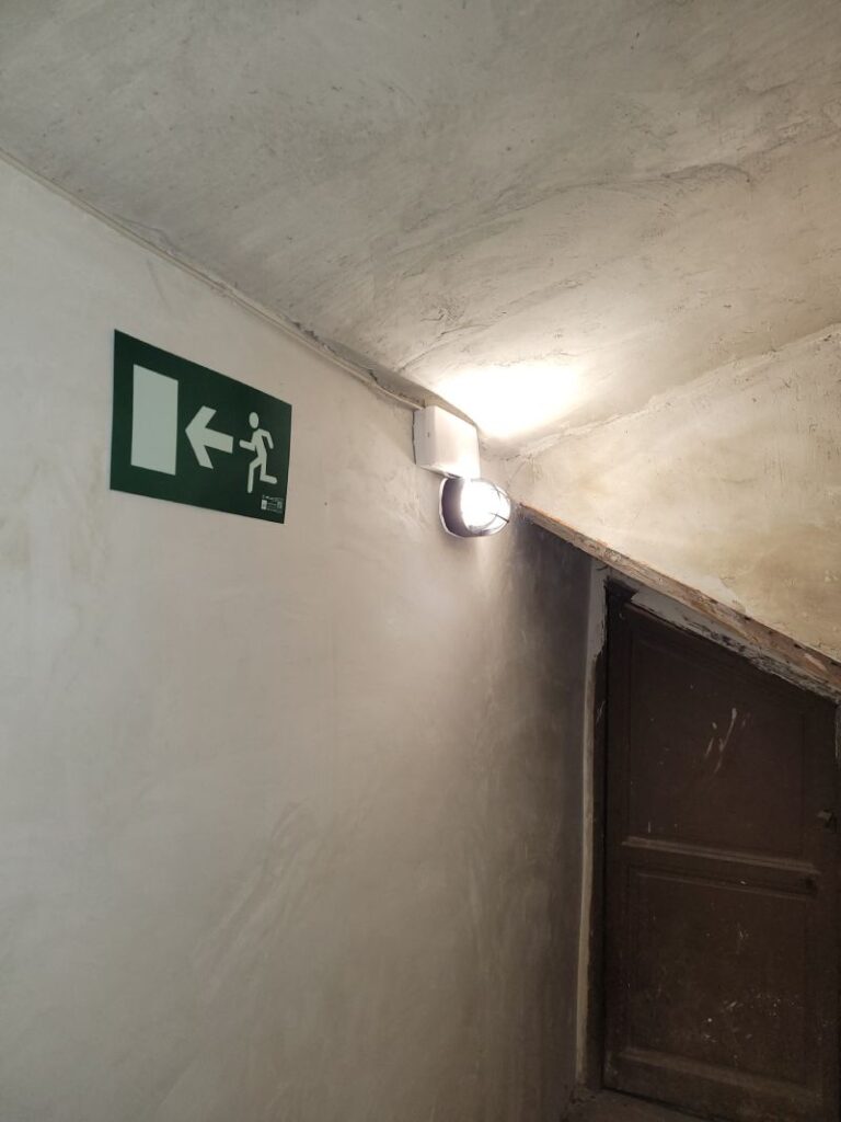 Caja de distribución eléctrica con un signo de advertencia de alto voltaje. El símbolo es un triángulo amarillo con un borde negro y un rayo negro en el centro. La caja es blanca y está montada en una pared.