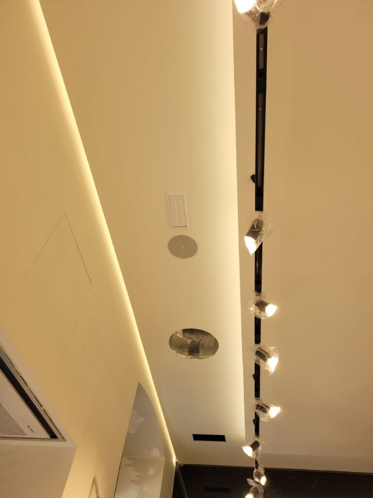 Techo de una habitación con una línea de focos colgantes y una instalación de ventilación. Las luces están empaquetadas y listas para ser instaladas, y el techo tiene un diseño moderno y limpio.
