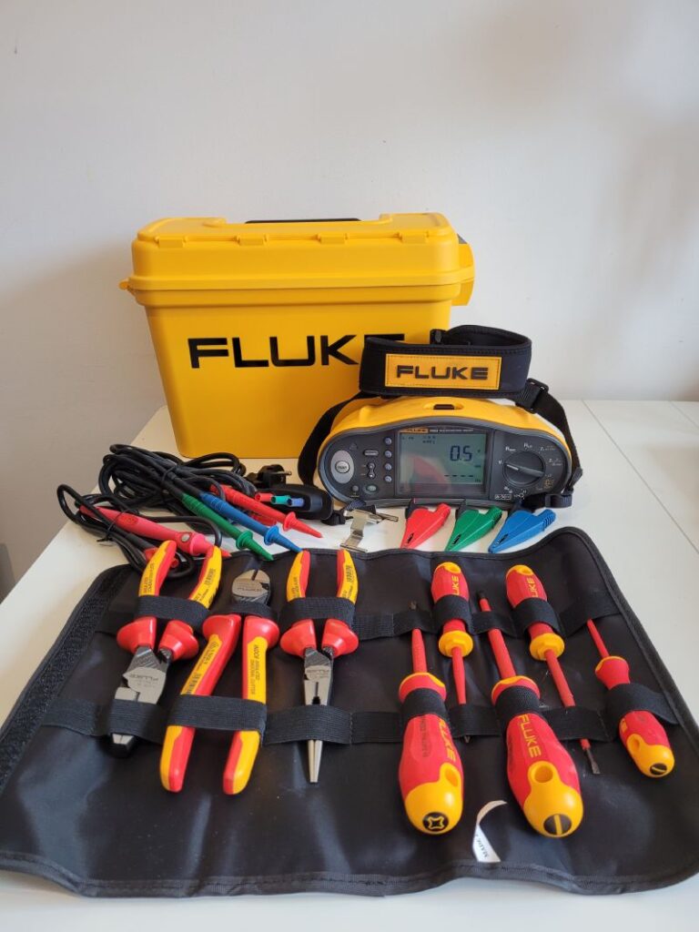 Un kit de herramientas de la marca Fluke, que incluye destornilladores, alicates y un multímetro. Las herramientas están organizadas en una bolsa de herramientas y hay una caja amarilla de Fluke en el fondo.