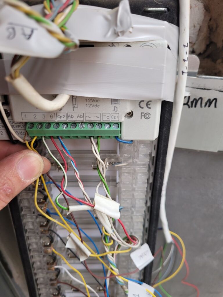 Un primer plano de un panel de control con varios cables de colores conectados a terminales. Los cables están etiquetados y hay una mano sosteniendo algunos de los cables para mostrarlos.