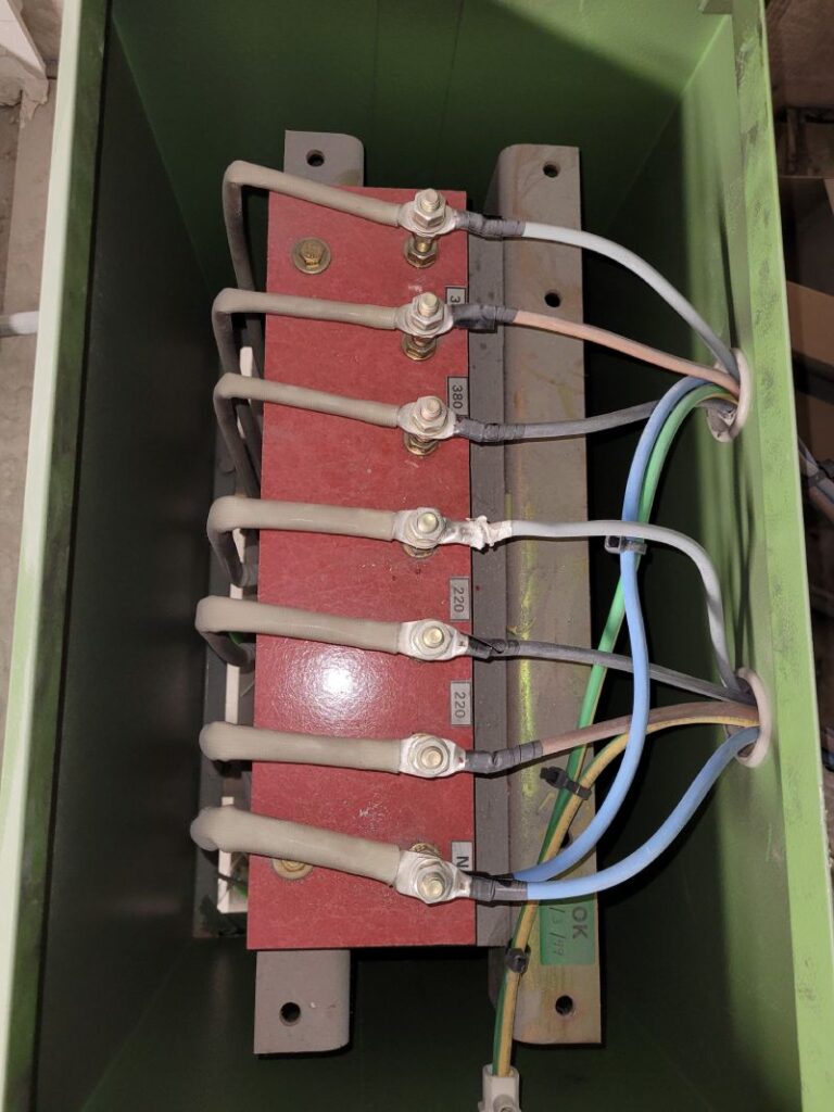 Caja de conexiones eléctricas con cables conectados a terminales en un panel rojo dentro de una estructura verde.