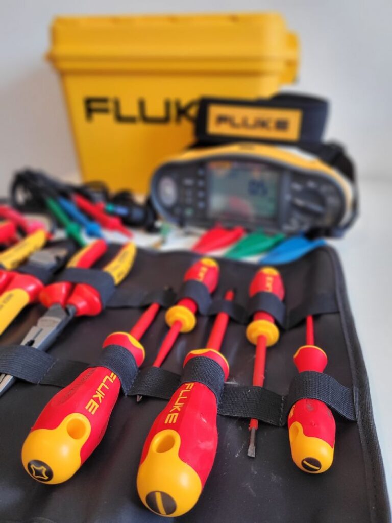 Un kit de herramientas de la marca Fluke, que incluye destornilladores, alicates y un multímetro. Las herramientas están organizadas en una bolsa de herramientas y hay una caja amarilla de Fluke en el fondo.